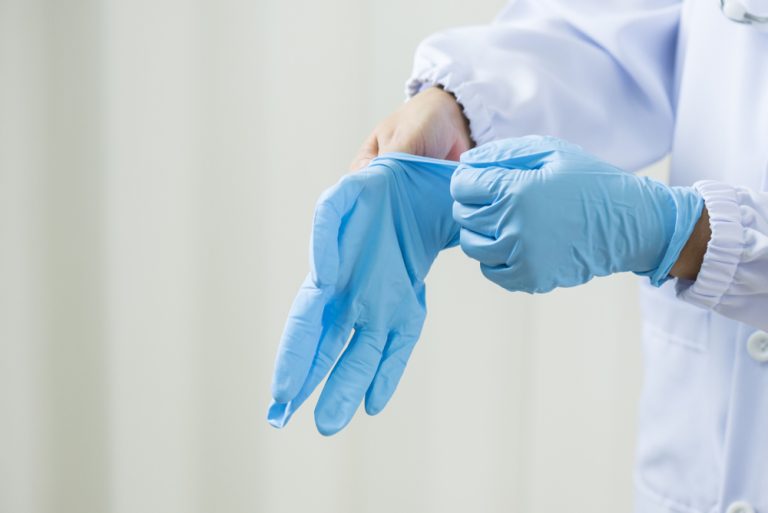 Женщина врач надевает латексные перчатки